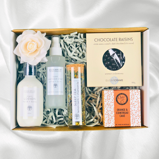 Sleep Gift Hamper containing sleep tea, lavender pillow spray, hand and body lotion, chocolate raisins and orange cointreau cake packed in a white gift box